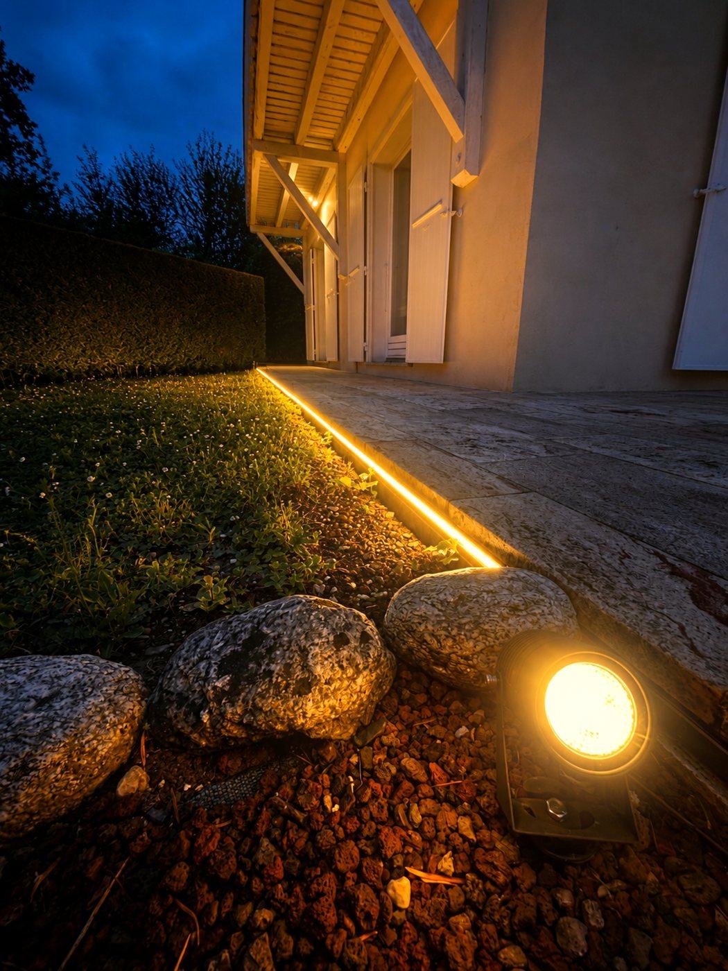 Ruban LED intégré le long d'une terrasse et projecteur d'accent sur galets